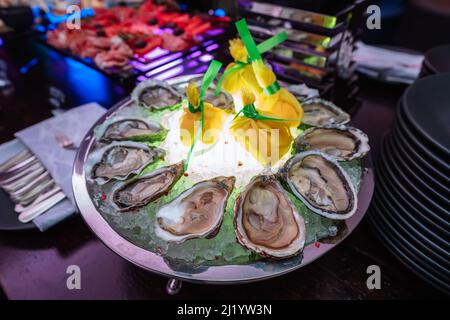 Frische Austern mit Limette auf Eis auf einem runden Teller. Austernsaison. Makrogericht mit Meeresfrüchten. Oyster auf der Halbschale Stockfoto