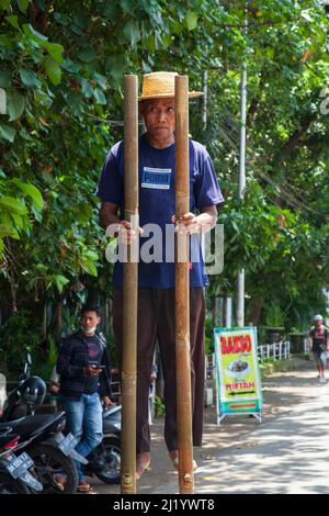 Ein älterer Mann, der auf Stelzen am Straßenrand in der Nähe von Denpasar Bali, Indonesien, unterwegs ist. Stockfoto