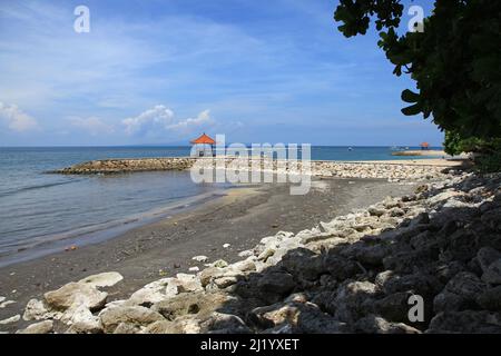 Blick auf den Strand und das Meer mit Wellenbrecher und kleinem Tempel im Norden von Sanur in Bali, Indonesien Stockfoto