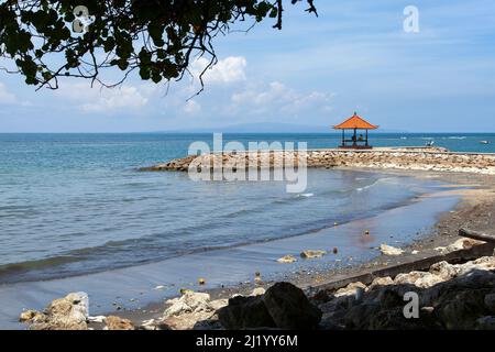 Blick auf den Strand und das Meer mit Wellenbrecher und kleinem Tempel im Norden von Sanur in Bali, Indonesien Stockfoto