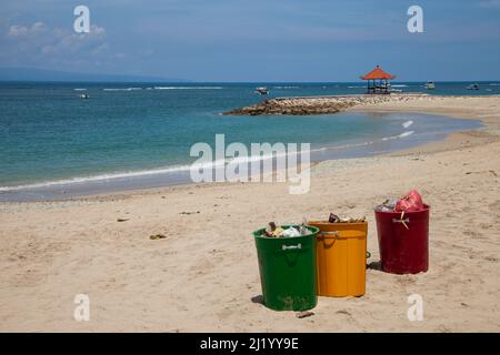 Blick auf den Strand im Norden von Sanur in Bali, Indonesien mit drei großen Mülltonnen auf dem Sand. Stockfoto