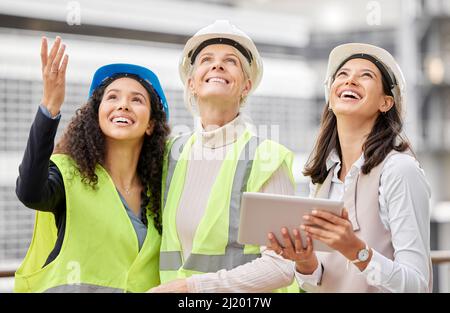 Vorstellung des Endprodukts. 3-fache Aufnahme von drei attraktiven Ingenieurinnen, die während der Arbeit auf einer Baustelle ein Tablet benutzten. Stockfoto