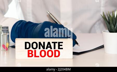 Das Wort Blutspende medizinisches Konzept in roten Buchstaben auf einem weißen Stück Papier in den Händen eines Geschäftsmannes geschrieben. Stockfoto