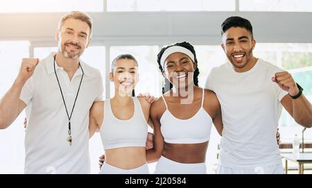 Das Siegerteam. Beschnittenes Porträt von drei jungen Tennisspielern und ihrem Trainer, der im Clubhaus steht und jubelt. Stockfoto