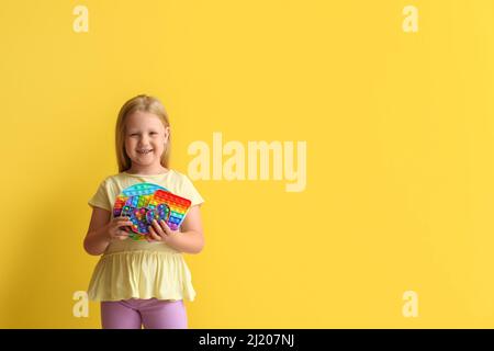 Glücklich kleines Mädchen halten Pop es fidget Spielzeug auf farbigem Hintergrund Stockfoto