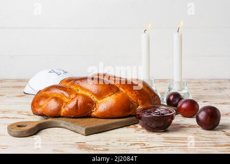 Traditionelles Challah-Brot mit glühenden Kerzen auf weißem Holzhintergrund. Shabbat Shalom Stockfoto
