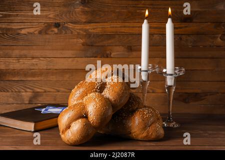 Traditionelles Challah-Brot mit glühenden Kerzen und Torah auf Holzgrund. Shabbat Shalom Stockfoto