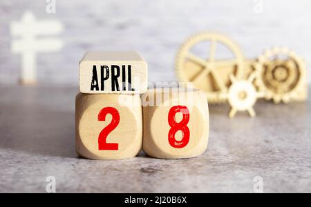 Kalender für April 28 : Würfel mit der Nummer 28, der Name des Monats April in englischer Sprache, ein Bouquet von blühenden Schneeglöckchen auf gelbem Hintergrund in Stockfoto