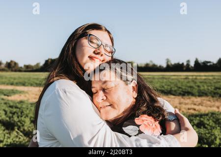 Großmutter und Enkelin umarmen sich an einem sonnigen Nachmittag mitten auf dem Feld. Familienportrait. Stockfoto