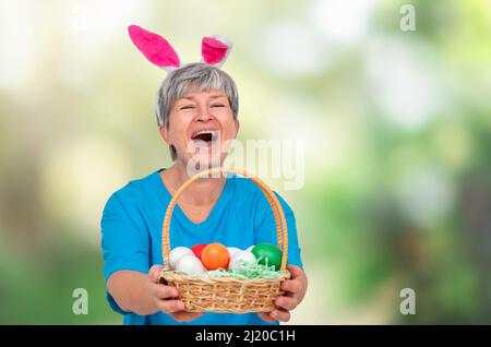 Ältere Frau in Hasenohren und mit osterkorb isoliert auf weißem Hintergrund Stockfoto