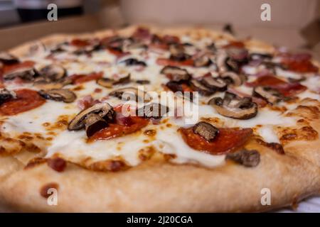 Makroökonomische, selektive Konzentration auf eine kitschige Lieferpizza, garniert mit frischen Pilzen und Pfefferoni in einem Karton Stockfoto