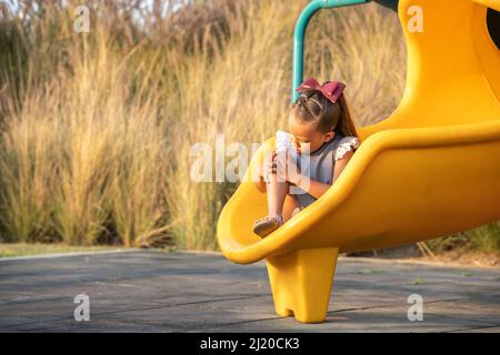 Kleines Mädchen mit verletzten Knie auf Rutsche im Park Stockfoto