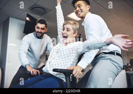 Mit einigen Kollegen Spaß im Büro. Aufnahme von Geschäftsleuten, die Spaß haben, indem sie ihre Kollegin mit auf ihren Stuhl im Büro nehmen. Stockfoto