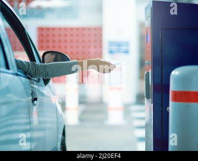 Das Leben in der Stadt hat seine Nachteile. Aufnahme eines nicht erkennbaren Fahrers, der ein Ticket in eine Parkuhr einführt. Stockfoto