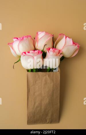 Zarte rosafarbene Rosen in einer Bastelpapiertasche auf beigem Hintergrund. Minimalistisch trendige Komposition. Abstrakte Kunstidee. Romantische rosa Rosenblüten in Pastelltönen. Moderne Ästhetik. Neutrale Erdtöne. Grußkarte Hintergrund Kopierbereich Banner Stockfoto