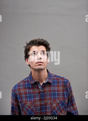 Es sieht aus wie Regen. Ausgeschnittene Aufnahme eines jungen Mannes, der im Freien steht und zum Himmel blickt. Stockfoto