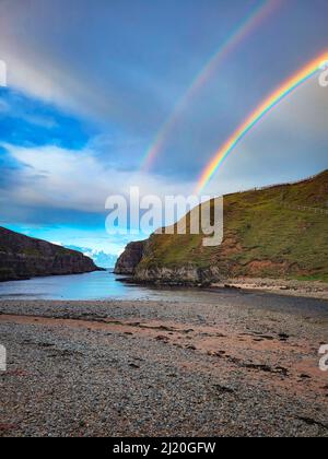 Eine malerische Aussicht auf den Regenbogen, der sich am blau bewölkten Himmel über der breiten Flussmündung in den Atlantischen Ozean in der Nähe der Smoo Cave, Durness, Schottland, zeigt Stockfoto