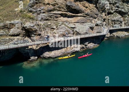 Radfahrer auf der Freischwinger-Brücke auf dem Lake Dunstan Cycle Trail und Kajakfahrer, Lake Dunstan, in der Nähe von Cromwell, Central Otago, Südinsel, Neuseeland - Drohne Stockfoto