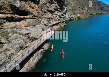 Radfahrer auf der Freischwinger-Brücke auf dem Lake Dunstan Cycle Trail und Kajakfahrer, Lake Dunstan, in der Nähe von Cromwell, Central Otago, Südinsel, Neuseeland - Drohne Stockfoto