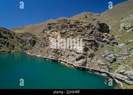 Radfahrer auf der Freischwinger-Brücke auf dem Lake Dunstan Cycle Trail und Kajakfahrer, Lake Dunstan, in der Nähe von Cromwell, Central Otago, Südinsel, Neuseeland - Drohne Stockfoto