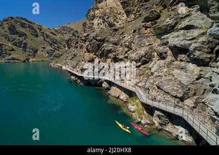 Radfahrer auf der Freischwinger-Brücke auf dem Lake Dunstan Cycle Trail und Kajakfahrer, Lake Dunstan, in der Nähe von Cromwell, Central Otago, Südinsel, Neuseeland - Drohne Stockfoto