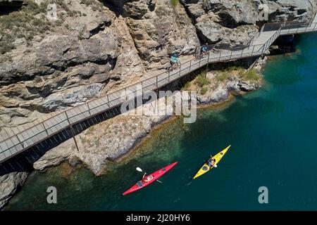 Radfahrer auf der Freischwinger-Brücke auf dem Lake Dunstan Cycle Trail und Kajakfahrer, Lake Dunstan, in der Nähe von Cromwell, Central Otago, Südinsel, Neuseeland - Drohne Stockfoto