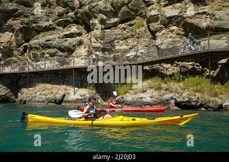 Radfahrer auf der Freischwinger-Brücke auf dem Lake Dunstan Cycle Trail und Kajakfahrer, Lake Dunstan, in der Nähe von Cromwell, Central Otago, Südinsel, Neuseelandl Stockfoto