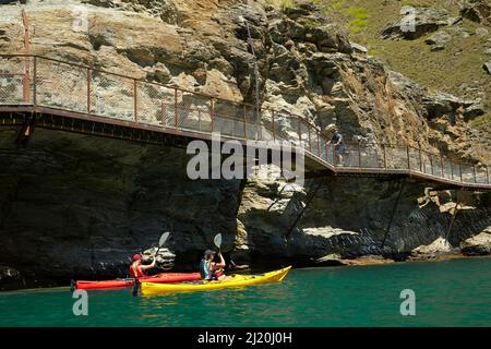 Radfahrer auf der Freischwinger-Brücke auf dem Lake Dunstan Cycle Trail und Kajakfahrer, Lake Dunstan, in der Nähe von Cromwell, Central Otago, Südinsel, Neuseelandl Stockfoto