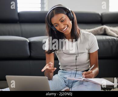 Oh, ich sehe, was du dort getan hast. Aufnahme einer jungen Frau, die in ihrem Wohnzimmer sitzt und Kopfhörer trägt, während sie ihren Laptop für einen Videoanruf verwendet. Stockfoto