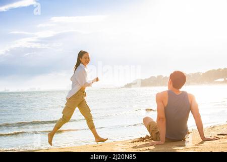 Ein junger Mann, der am Strand sitzt und eine junge Frau anschaut - Stockfoto Stockfoto