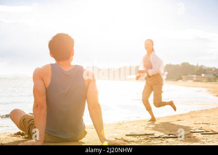 Ein junger Mann, der am Strand sitzt und eine junge Frau anschaut - Stockfoto Stockfoto