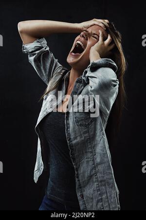 NOOOO Lassen Sie mich in Ruhe. Eine junge Frau, die unkontrolliert schreit, während sie auf schwarzem Hintergrund isoliert ist. Stockfoto