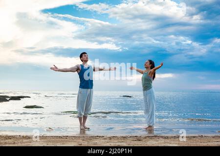 Junges Paar, das Yoga-Meditation praktiziert, während es am Strand steht - Stock photo Stockfoto