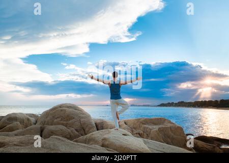 Muskulöser junger Mann, der Yoga auf einem Strandfelsen macht - Stock Photo Stockfoto