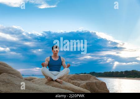 Muskulöser junger Mann, der auf einem Strandfelsen meditiert - Stock Photo Stockfoto