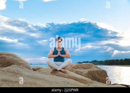 Muskulöser junger Mann, der auf einem Strandfelsen meditiert - Stock Photo Stockfoto