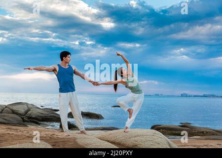 Paare, die Yoga auf den Felsen der Insel praktizieren - Stock photo Stockfoto