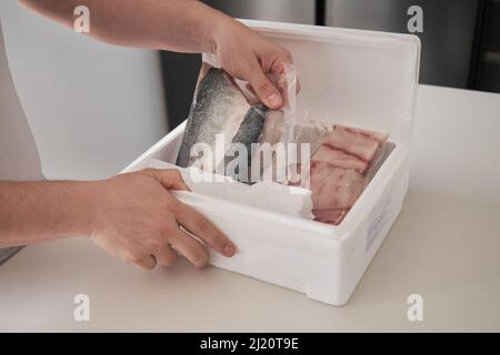 Nicht erkennbarer Mensch, der seine wöchentliche Lieferung von Fischen in einer isothermen Kiste öffnet. Stockfoto