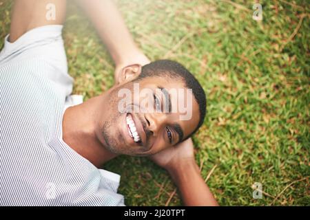 Ich habe die ganze Woche auf diesen Moment gewartet. Aufnahme eines jungen Mannes, der sich im Freien auf dem Gras entspannt. Stockfoto
