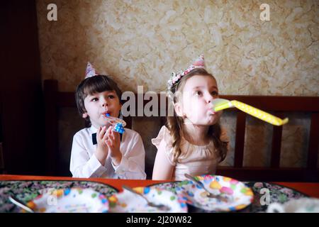 Kinderparty in Mützen feiert Geburtstag mit Kuchen und Ballons zu Hause. Stockfoto