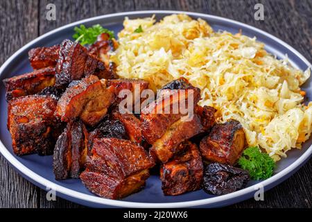 Nahaufnahme von geschmortem Sauerkraut mit Schweinefleisch und Pflaumen auf dem Teller auf dem Holztisch Stockfoto