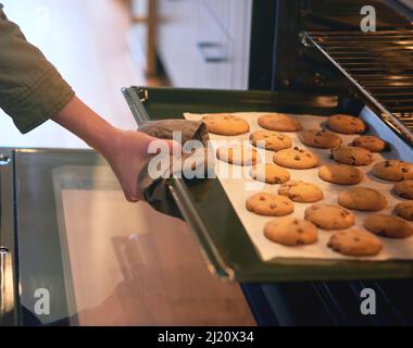 Nichts riecht besser als selbstgebackene Kekse. Ein kurzer Schuss einer unkenntlichen Frau, die Cookies aus dem Ofen nimmt. Stockfoto