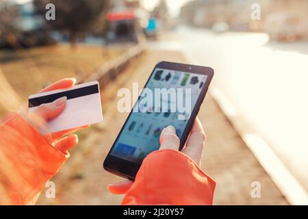 Das Konzept des Online-Shoppings. Die Hände der Frauen halten ein Smartphone mit unscharfem Bildschirm und eine Bankkarte, die online im Online-Shop einkaufen. Stockfoto