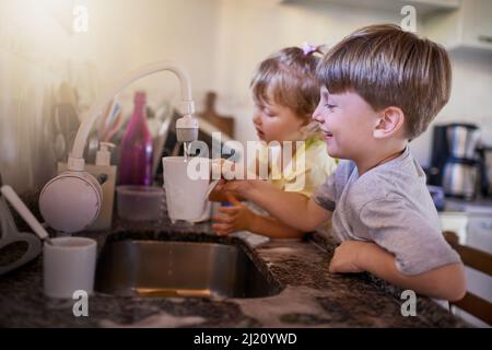 Sie werden super sauber sein, wenn sie fertig sind. Aufnahme von zwei liebenswerten kleinen Geschwistern, die in der Küche zu Hause gemeinsam Geschirr waschen. Stockfoto