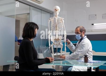 Physiotherapeutin zeigt der Frau im Schrank Gelenk am menschlichen Skelett. Spezialist erklärt Knochenschmerzen und Diagnose an Patienten mit Verletzung, spricht über Osteopathie und Anatomie. Stockfoto