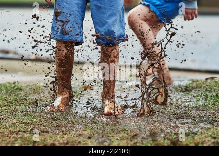 Sei jung, mach ein Chaos. Low-Angle-Aufnahme von zwei nicht erkennbaren Kindern, die an einem regnerischen Tag im Schlamm herumspringen. Stockfoto