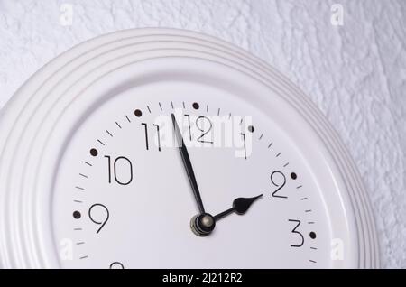 Weiße Uhr mit schwarzen Zeigern an einer Wand im Innenbereich Stockfoto