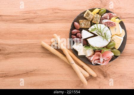 Charcuterie-Tafel mit einer Auswahl an Käse, Wurst und Prosciutto, serviert zusammen mit Oliven und Brotscheiben auf schwarzem Teller auf einem Holztisch. Ital Stockfoto