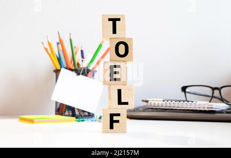 TOEFL - Wörter aus Holzblöcken mit Buchstaben, der Test des Englischen als Fremdsprache, TOEFL-Konzept, weißgrauer glänzender Hintergrund mit Reflexion Stockfoto