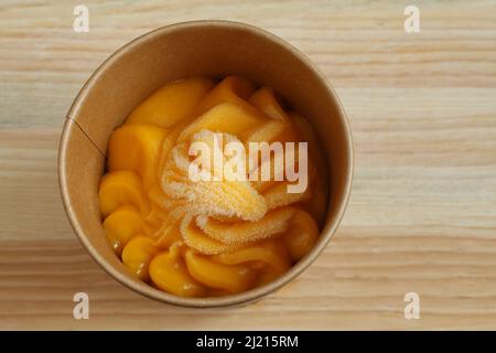 Mango Sorbet in einem Pappbecher steht auf einem Holztisch. Nahaufnahme. Draufsicht Stockfoto